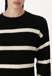 Suéter de malha preto com riscas horizontais em creme, gola redonda e tecido texturizado. Close-up da seção superior e da gola.