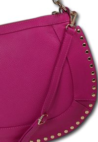 Fuchsia leren tas met een gestructureerde afwerking, voorzien van gouden studs aan één kant en een afneembare schouderband. Ritsafsluiting aan de bovenkant.