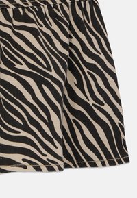 Zebra-mønstret stoff med svarte striper på en beige bakgrunn. Materialet virker robust med synlige sømmer nederst.