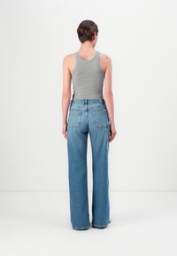 Grå ribbet singlet kombinert med høyt liv, vide blå denimjeans med baklommer og en liten sidelomme.