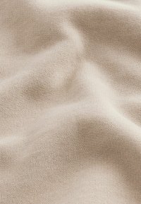 Tessuto a maglia beige con una trama fine, caratterizzato da sottili variazioni di tonalità. Il materiale appare morbido e leggermente allungato.