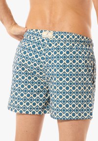 Bañadores de hombre con un diseño estampado que presenta diamantes y círculos en tonos azul y crema. Cintura elástica con una etiqueta de logo en la parte trasera.