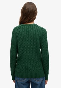 Zielony sweter w sploty z teksturowanym wzorem, raglanowymi rękawami i prążkowanym dołem. Na lewym rękawie małą metką z amerykańską flagą.