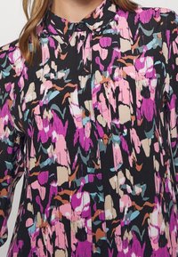 Camicia nera con un motivo astratto colorato nei toni del rosa, teal e beige; presenta un colletto alla francese e bottoni lungo la parte anteriore.