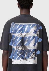 Sort t-shirt med et stort grafisk print og blå tekst "WAVE" over et monochromt billede af bølger på ryggen. Korte ærmer, afslappet pasform.