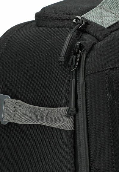 Bolsa de tela negra con superficie texturizada, cuenta con una correa gris, cierre de cremallera y gancho, diseñada para la durabilidad y funcionalidad.
