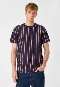 Camiseta de marina con rayas rojas y blancas verticales, cuello redondo y mangas cortas, combinada con unos vaqueros de mezclilla. Material de algodón, corte casual.