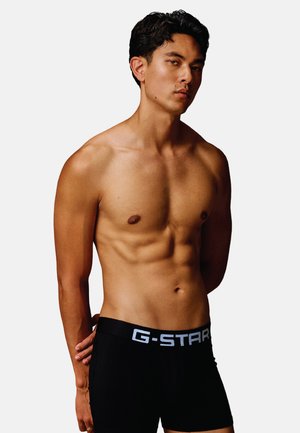 Boxer-briefs G-Star noirs avec un logo blanc sur la ceinture, tissu lisse, design ajusté et taille basse, modèle les portant.