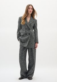 Pelēks un balts houndstooth kostīms ar dubultā krūšu žaketi ar lielām pogām un plašiem biksēm. Gluda tekstūra un piegriezums.