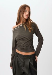 Mørke olivengrøn langærmet skjorte med en rynket design og off-the-shoulder stil, der har sølvfarvede øjer detaljer ved halsudskæringen.