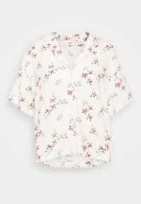 Chemise blanche à manches courtes avec col pointu et motif floral rose et vert.