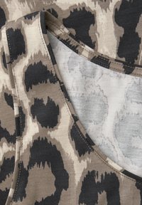 Gros plan sur un tissu imprimé léopard beige et noir avec des coutures visibles et des bords pliés.