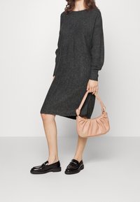 Grå ulltröja klänning med lös passform och långa ärmar, i kombination med en ljusrosa läderhandväska och svarta lackskor.