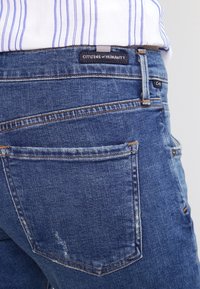 Blå denimjeans från Citizens of Humanity med en lätt sliten textur, med en klassisk femfickdesign och en baketikett.