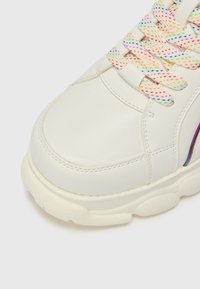 Baskets en cuir blanc avec un bout rond, présentant des lacets colorés et mouchetés ainsi qu'une semelle texturée et épaisse. Accent latéral en violet.