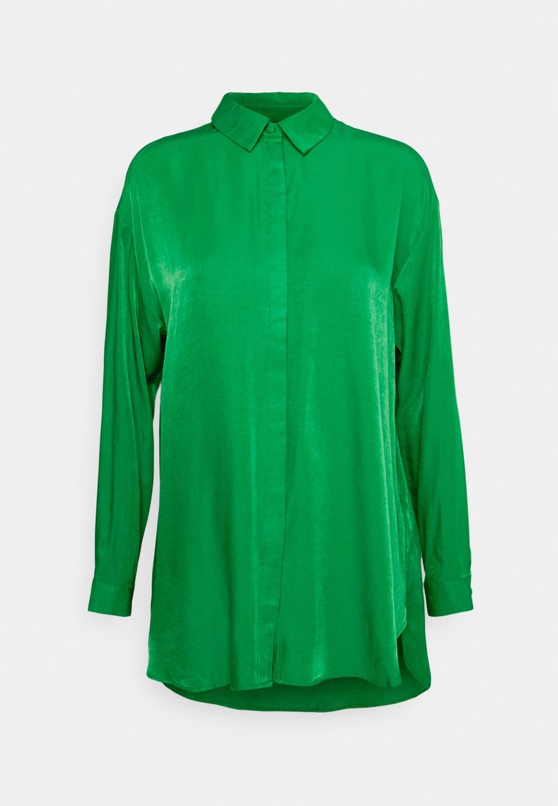 Grön skjorta med långa ärmar, tillverkad av ett slätt, glänsande tyg. Har en spetsig krage och knappstängning, med en lätt rundad nederdel.