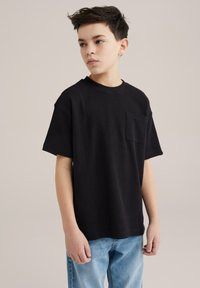 Svart t-shirt med kort ärm i ett strukturerat tyg, med en bröstficka, kombinerat med ljusblå denimjeans.