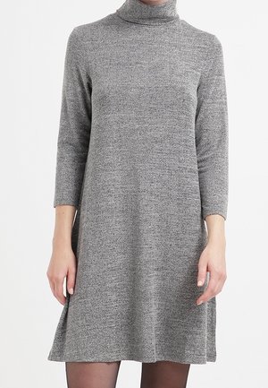 Vestito grigio a collo alto lavorato a maglia con maniche a tre quarti, indossato da una persona che sta in piedi davanti a uno sfondo bianco semplice.