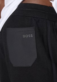 Svarta träningsbyxor med en texturerad svart ficka med "BOSS" präglat. Elastisk midja för ökad komfort och flexibilitet.