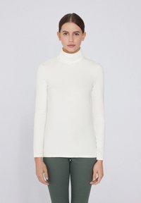 Camisa de manga larga blanca tipo cuello alto, hecha de una tela suave, con un diseño ajustado y un cuello alto. Sin patrones visibles ni adornos.