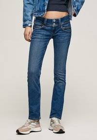 Sittende blå jeans med en jevn tekstur, fem lommer og sømdetaljer. Kombinert med grå og rosa joggesko med polstret såle.