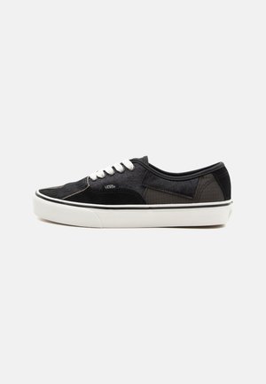 Black canvas sneakers featuring contrasting textures, white laces, and a rubber sole. Includes a patterned side accent and logo detail.