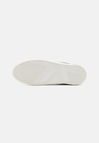 Hvit sneakersåle med en teksturert gummioverflate med horisontale og diagonale spor for grep; minimalistisk design uten logoer.