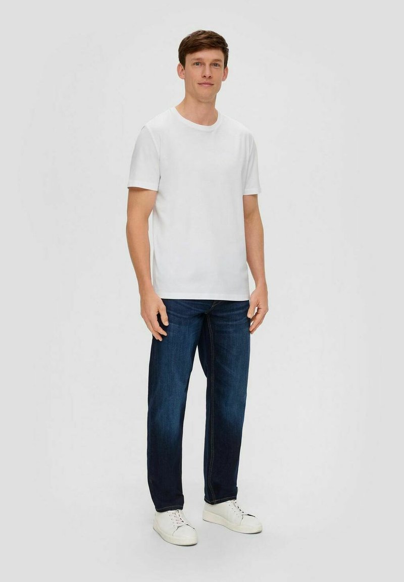 Weißes Baumwoll-T-Shirt mit kurzen Ärmeln, kombiniert mit dunkelblauen Jeans und weißen Sneakers. Schlichte, klassische Passform ohne sichtbare Muster.