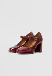 Bottines à talons Mary Jane en cuir verni bourgogne avec un bout carré, une bride de cheville ajustable et un talon épais. Fini lisse et brillant.