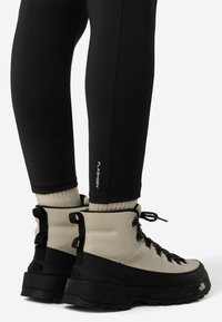 Ľahké trekingové topánky v béžovej a čiernej farbe s textúrovaným zvrškom, šnúrkami a gumovou podrážkou. Čierne legíny s bielym logom "FLASHDRY".