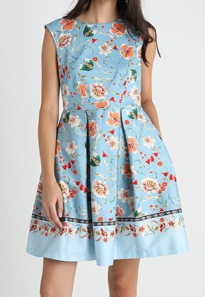 Ärmelloses hellblaues Kleid mit orangefarbenen, weißen und roten Blumenmustern und einem plissierten Rock, getragen von einer stehenden Person.