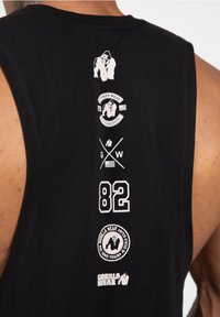 Zwarte tanktop met meerdere witte logo's, waaronder 'Gorilla Wear', het nummer '82', en gorilla-illustraties. Glad stofoppervlak.