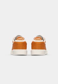 Orange suede sneakers with white rubber soles, featuring a padded collar and logo at the back. Smooth texture with a classic low-top design.