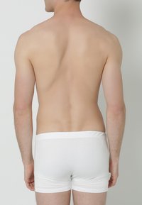 Witte katoenen boxershorts met een elastische tailleband, weergegeven op een persoon die zich van de camera afwendt, waarbij de achterkant en zijprofiel zichtbaar zijn. Gladde textuur.