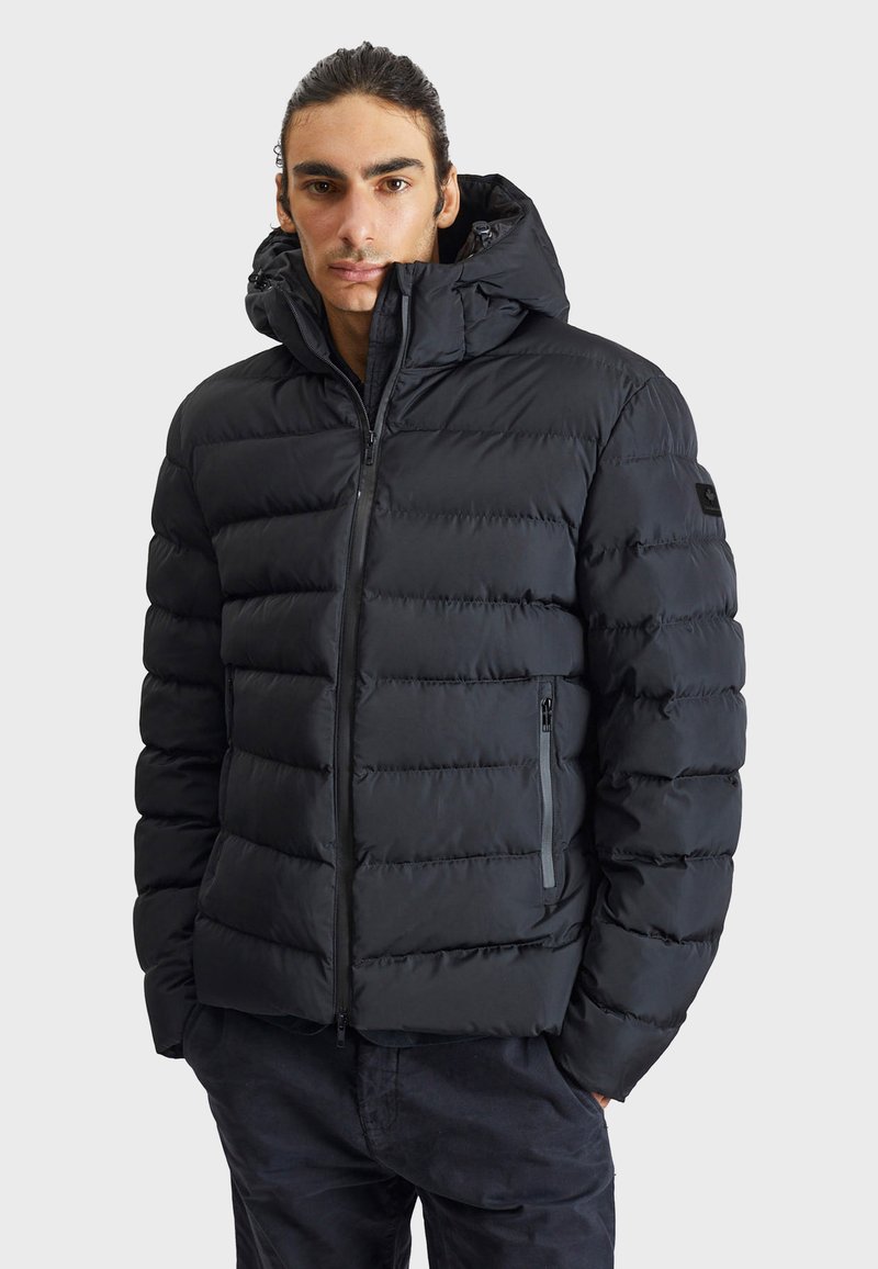 Black puffer jacket with a zip-up front, large hood, and horizontal quilted texture. Features side pockets and subtle branding on the sleeve.