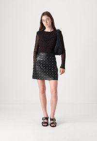 Svart, mesh langermet topp med røde prikker, kombinert med et svart skinn miniskjørt prydet med sølvstifter. Tilbehør med en teksturert veske.