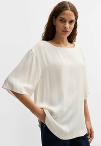 Blusa bianca leggera con vestibilità ampia, maniche larghe e scollo a barchetta, con un sottile motivo texturizzato.