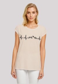Light beige t-shirt with a relaxed fit, short sleeves, and a black heart rate line graphic featuring mountain silhouettes across the chest.