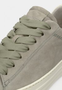 Γκρι σουέντ αθλητικό παπούτσι με κορδόνια ελιάς, στρογγυλή μύτη, διακριτικές ραφές και κρέμ καουτσουκένια σόλα. Η υφή φαίνεται απαλή και λεία.