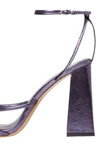 Sandalo alto in metallo viola con tacco a blocco, cinturino alla caviglia e design minimalista. Presenta una texture liscia e linee semplici.