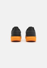 Des chaussures de course noires avec une semelle orange, dotées d'un dessus texturé et d'un col rembourré, conçues pour le confort et la stabilité.