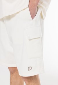 Lysecreme cargo shorts lavet af bomuldsblandingsstof. Har sidelomme og broderet logo nær kanten. Casual, afslappet pasform.