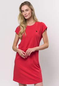 Rochie roșie din bumbac, cu mâneci scurte, decolteu rotund, detaliu cu nasture la talie și un mic logo negru pe piept. Textură netedă și croială casual.