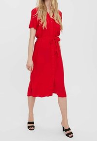 Punainen, lyhythihainen napitettava mekko, jossa on solmittava vyötärö. Sisältää sivurei'ät ja kunnianhimoisen siluetin. Yhdistetty mustien avonaisen kärjen korkokenkien kanssa.