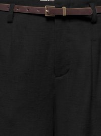 Gros plan sur un pantalon noir texturé avec une ceinture en cuir marron avec une boucle rectangulaire dorée.
