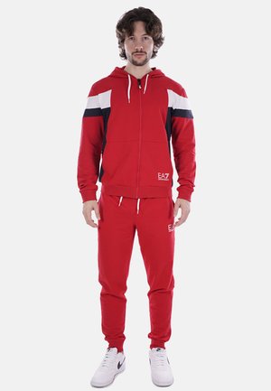 Felpa con zip rossa e pantaloni jogger coordinati realizzati in tessuto misto cotone. Presenta strisce a contrasto bianche e blu navy. Dotata di lacci e logo.