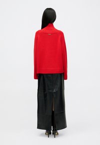 Red knitted sweater with a high collar and ribbed hem, paired with a black leather maxi skirt featuring a back slit. Black high-heel boots.