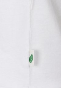 Tissu blanc à texture lisse présentant une petite étiquette en tissu ornée d'un motif de feuille verte, placée près de la couture latérale.