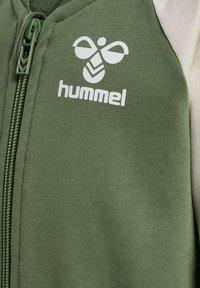 Groene zip-up jas met een wit logo op de borst en contrasterende lichtgekleurde schouderpanelen. Gemaakt van zachte, gestructureerde stof.