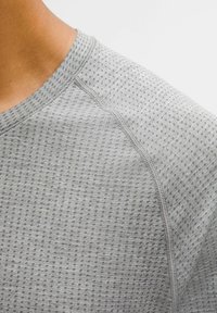 Tricou gri cu mâneci scurte, confecționat dintr-un material texturat cu modele mici punctate, cu guler rotund cu refilet și cusături plate.